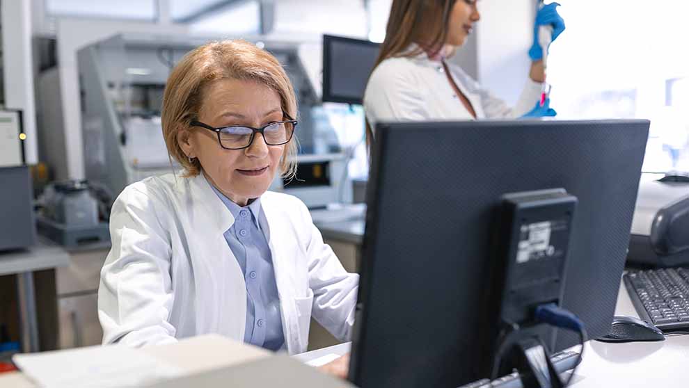 lab manager looks at screen accessing lab management software while lab assistant looks at sample