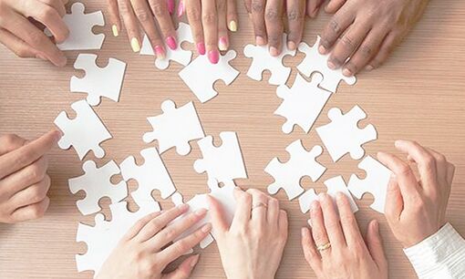 multiple people arrange white puzzle pieces on a table