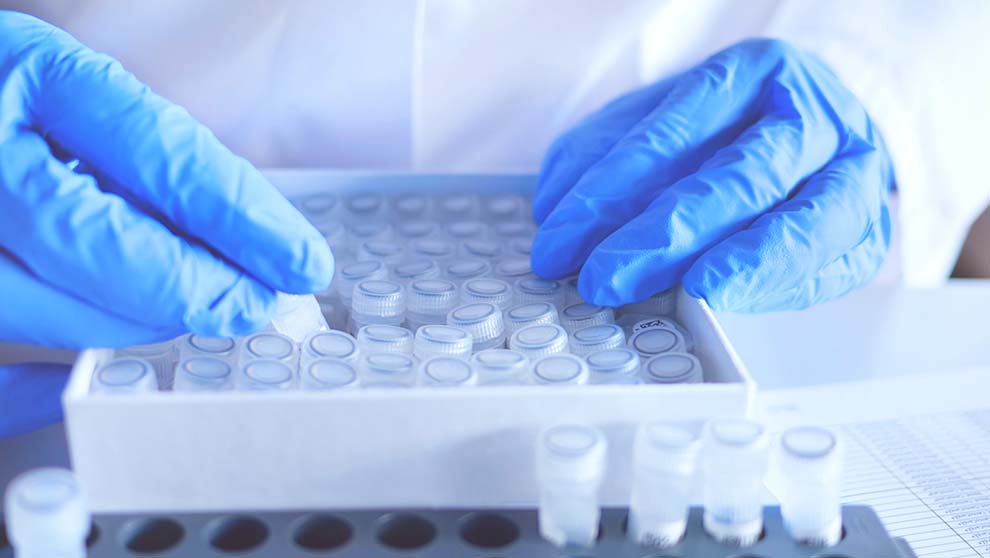 gloved hands rifle through tray of 15 ml lab specimen tubes
